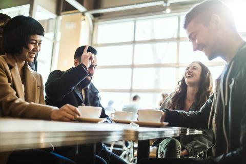 Four people laughing while seated around a tabel with coffee cups